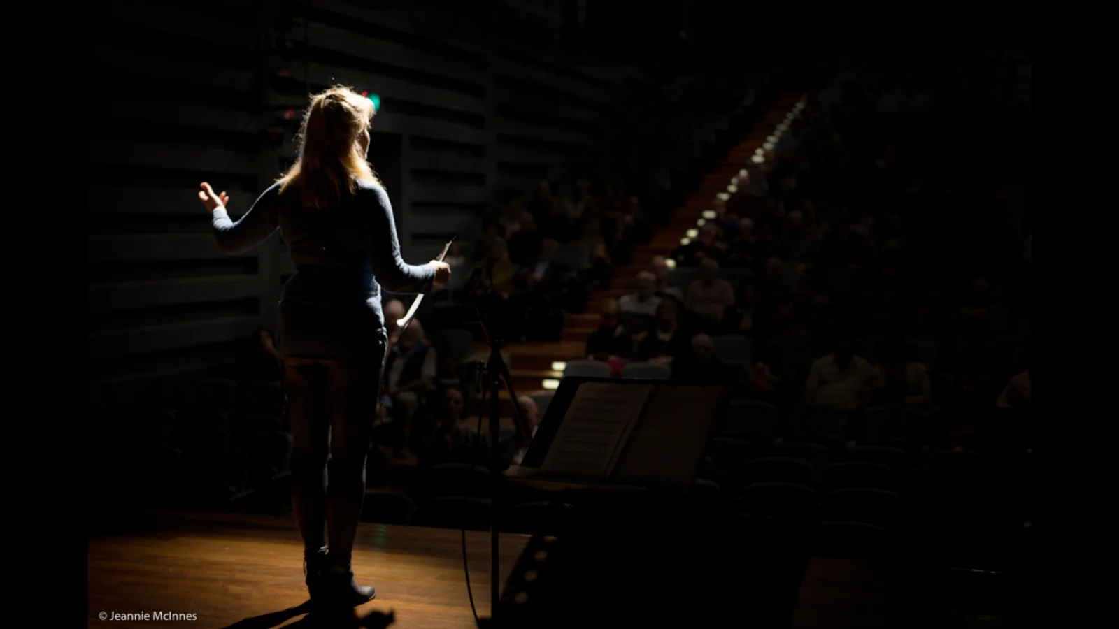 Annabelle Drumm presenting on stage at The Joan, Sydney, with audience in darkened auditorium