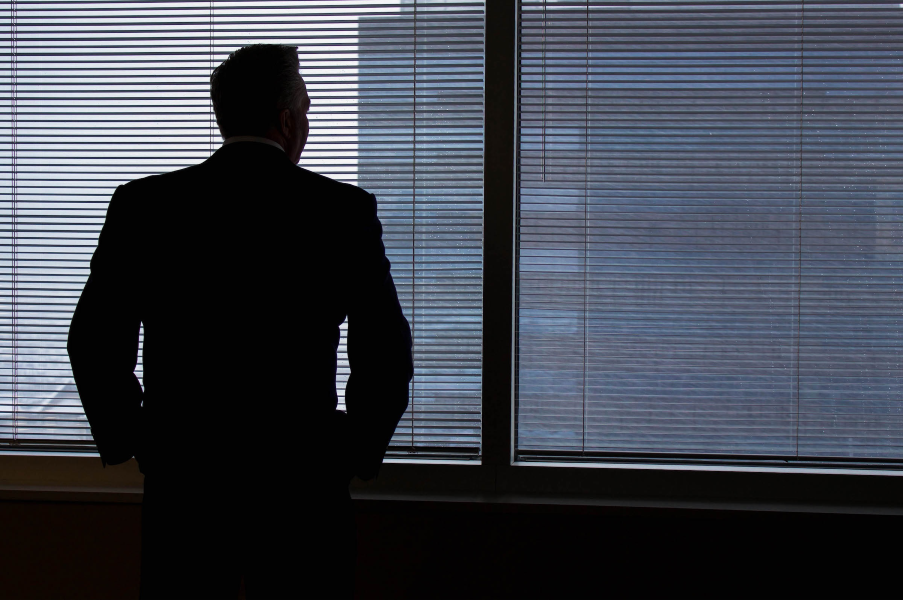 Business professional standing at the window, looking out over the city — contemplating a graceful transition